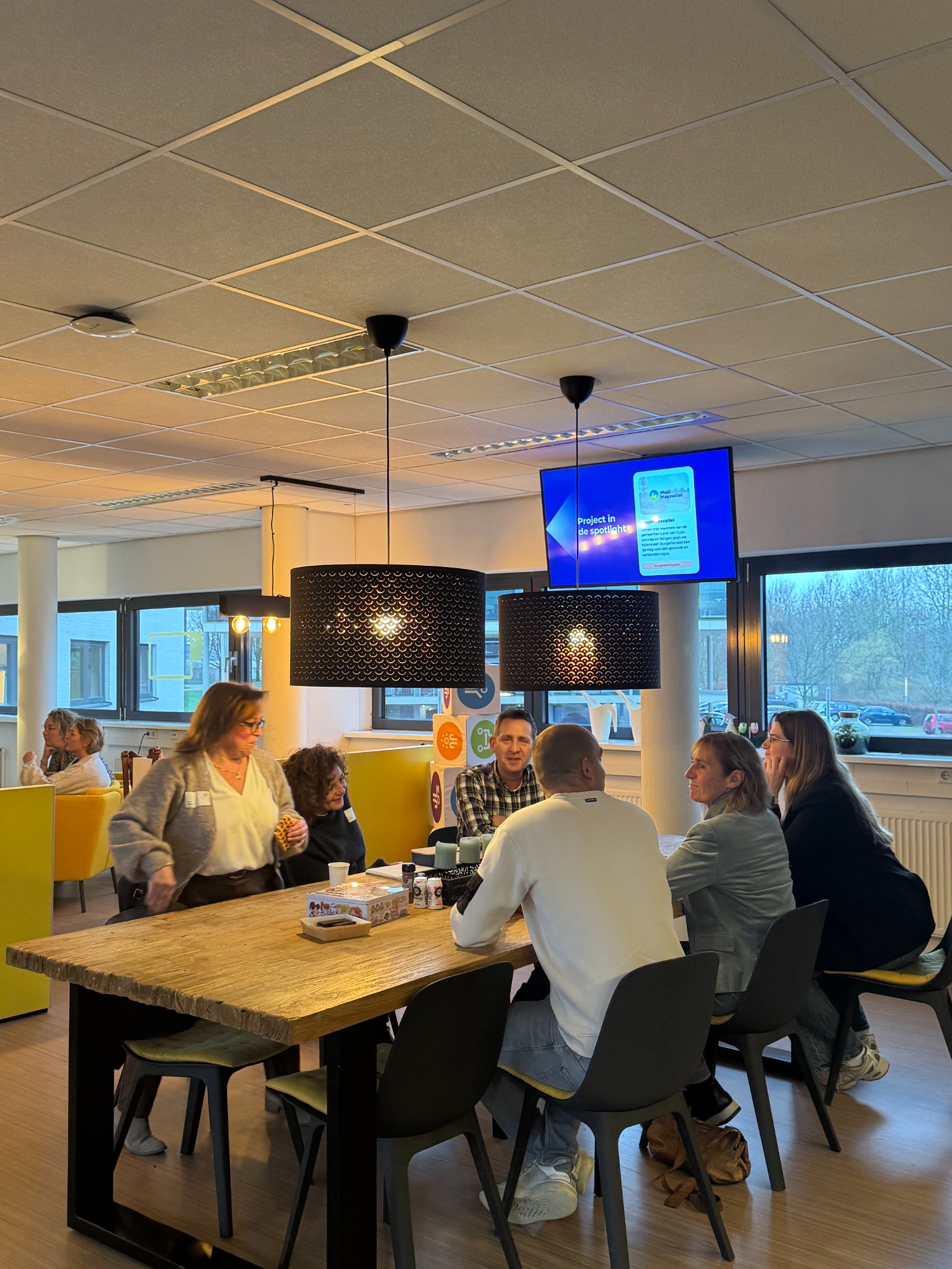 Deelnemers aan een Bij VIC-bijeenkomst in gesprek aan een houten tafel.